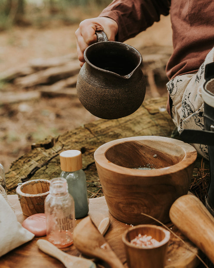 Child sitting outdoors mixing potions from the Wild Adventure kit on a tree trunk