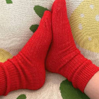 Bed and Butter cosy red ankle socks styled against white waffle and boucle cushions