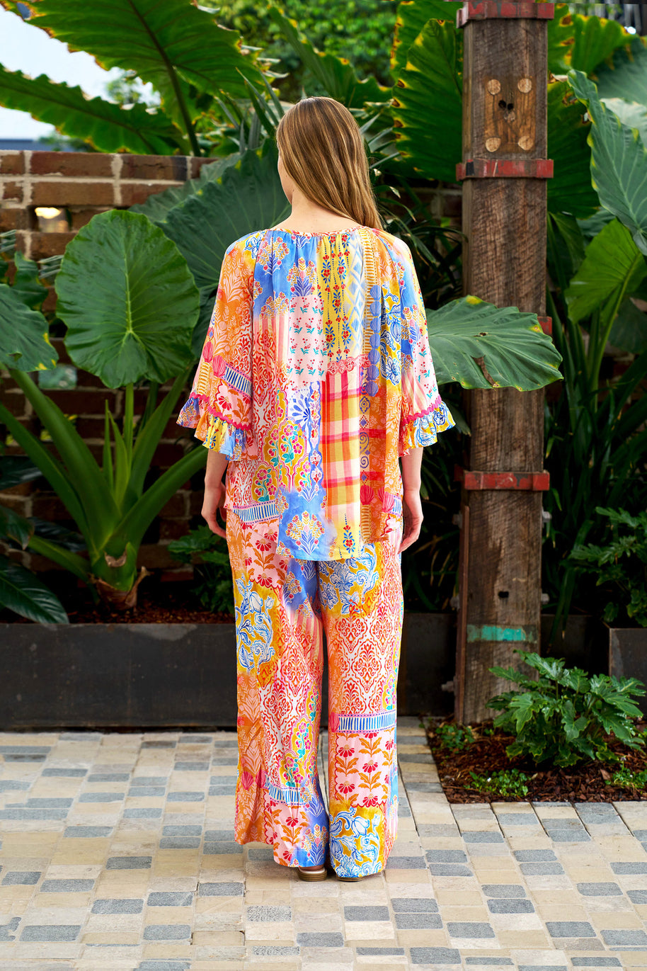 Model wearing the Alizee Top in a colourful multi patch print with 3/4 ruffled sleeves and tie neckline.