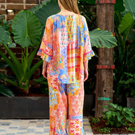 Model wearing the Alizee Top in a colourful multi patch print with 3/4 ruffled sleeves and tie neckline.