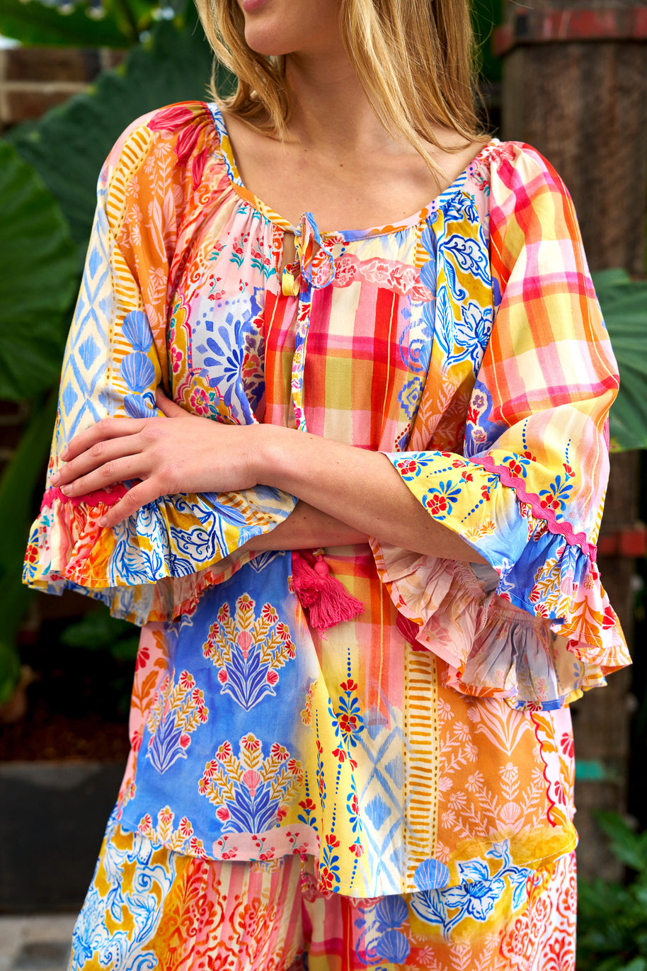 Model wearing the Alizee Top in a colourful multi patch print with 3/4 ruffled sleeves and tie neckline.