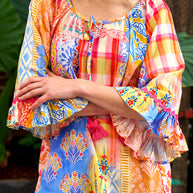Model wearing the Alizee Top in a colourful multi patch print with 3/4 ruffled sleeves and tie neckline.