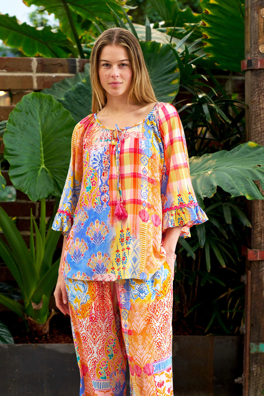 Model wearing the Alizee Top in a colourful multi patch print with 3/4 ruffled sleeves and tie neckline.
