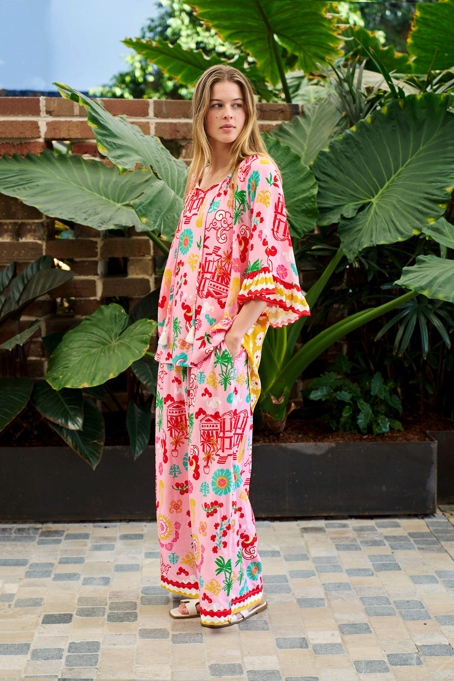 Model wearing the Mercedes Top in Pink Yellow featuring a tie neckline, 3/4 bell sleeves and a bold multicolour print.