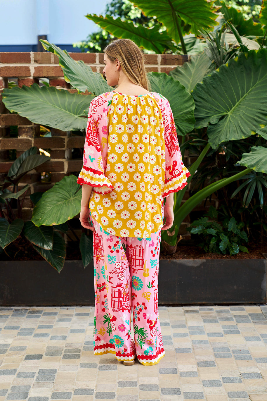 Model wearing the Mercedes Top in Pink Yellow featuring a tie neckline, 3/4 bell sleeves and a bold multicolour print.