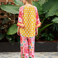 Model wearing the Mercedes Top in Pink Yellow featuring a tie neckline, 3/4 bell sleeves and a bold multicolour print.