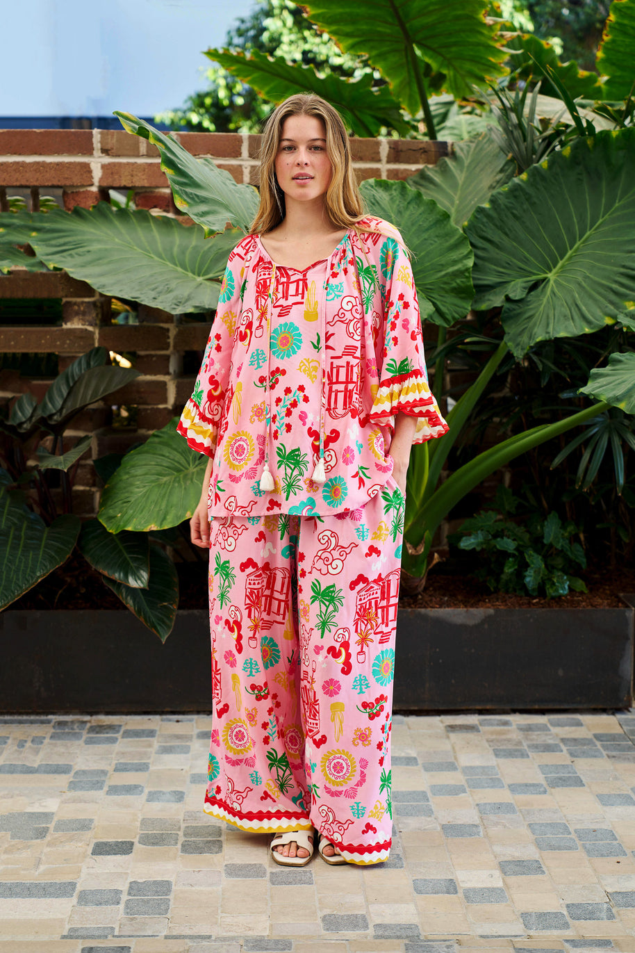 Model wearing the Mercedes Top in Pink Yellow featuring a tie neckline, 3/4 bell sleeves and a bold multicolour print.