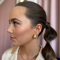 Flat gold stud earring worn on an ear